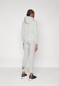 Haut à capuche gris avec une poche kangourou, leggings gris assortis et chaussures de sport noires avec accents jaunes. Tissu simple et lisse, coupe décontractée.
