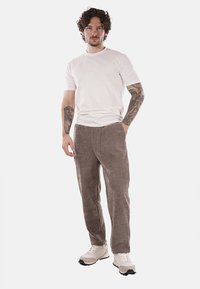 Pantaloni in corduroy marrone con taglio dritto, abbinati a una maglietta bianca semplice e sneakers beige, con dettagli visibili delle cuciture e della texture.
