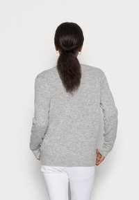 Szary sweter z dzianiny z długimi rękawami, okrągłym dekoltem i prążkowanymi detalami przy mankietach oraz u dołu. Nosi się go na białych spodniach. Miękka tekstura.