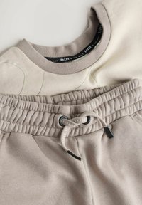 Light beige sweatshirt with textured neckline and subtle pattern paired with soft beige joggers featuring an elastic waistband and drawstring.