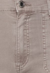 Tecido de ganga rosa claro com design clássico de cinco bolsos, costuras quilffcadas e fecho de botão prateado. Textura suave com ligeiro brilho.