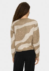 Brūns un krēms ar rakstu svārku ar teksturētu apdari, ar plašu kakla izgriezumu un ribotu apakšu, savienots ar melniem biksēm.