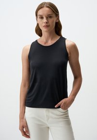 Top nero senza maniche realizzato in tessuto morbido con scollatura rotonda, vestibilità rilassata e una leggera lucentezza. Abbinato a pantaloni di colore chiaro.