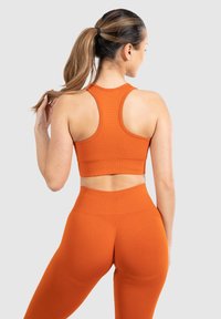Sujetador deportivo de rayas naranja y leggings de cintura alta, diseño sin costuras, ajustados, con detalles texturizados a lo largo de la espalda.