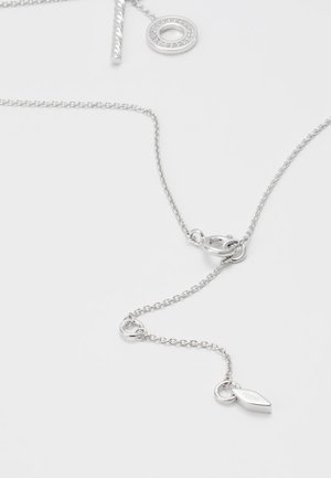 Chaîne de collier en argent avec un fermoir à bascule et un petit pendentif gravé portant l'inscription "Fossil" sur un fond clair.