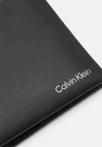 Černá kožená peněženka s hladkou strukturou a stříbrným vyraženým logem "Calvin Klein" v dolním pravém rohu.