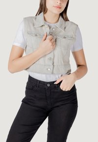 Gilet di denim grigio chiaro, tagliato, con bottoni frontali, tasche sul petto e design con colletto, indossato sopra una t-shirt bianca e pantaloni neri.