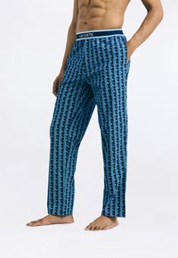 Pantalones de pyjama azuis com um padrão geométrico, apresentando um cós preto com o logótipo "LACOSTE". Feitos de tecido suave.