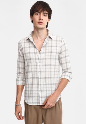 Camicia a quadri bianca e grigia con colletto button-down, maniche arrotolate e in tessuto leggero. Presenta una vestibilità rilassata e bottoni bianchi.