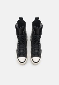 Svarte høye sneakers med en skinnende lærutside, rund tåhette og teksturerte lisser. Har en myk fôr og solid såle.