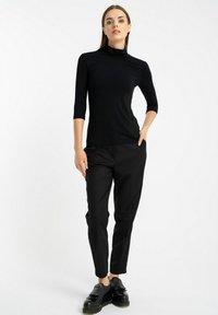 Czarna dopasowana bluzka z wysokim kołnierzem i rękawami o długości trzech ćwierć, w połączeniu z czarnymi zwężającymi się spodniami i czarnymi loafersami z frędzlami. Gładka faktura.