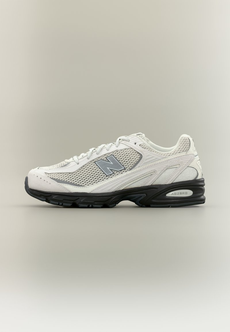 Baskets blanches New Balance avec des panneaux en mesh gris, une semelle noire et le logo "N" sur le côté, présentées sur un fond uni.