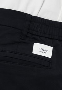 Σορτς από μπλε ναυτικού υφάσματος με ελαστική μέση και λευκή ετικέτα με τα γράμματα "REPLAY" και "SINCE 1981" στην πίσω τσέπη.