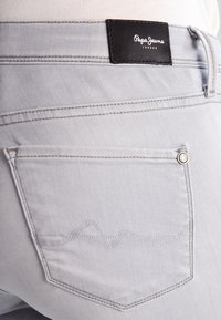Los jeans de mezclilla gris claro presentan un diseño de bolsillo cosido, una etiqueta de cuero negro con "Pepe Jeans London" y acentos de costura en contraste.