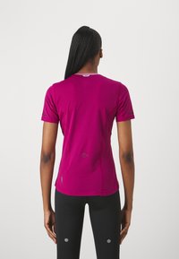 Camisa ajustada de manga corta en un vibrante magenta, con un tejido texturizado que presenta sutiles detalles de malla y acentos reflectantes en las mangas.