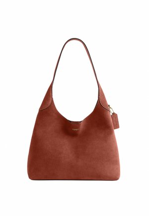 Sac à main Coach en daim marron avec une bandoulière unique et une petite étiquette suspendue, design minimaliste, texture lisse et détails en métal doré.