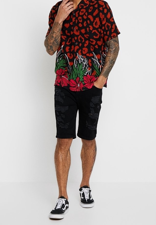 Homme portant une chemise à manches courtes rouge et noire à imprimé floral animalier, un short noir déchiré et des baskets noires et blanches.
