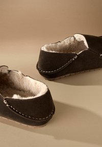 Brune ruskind slippers med pelsfor, elastisk åbning og stikninger. Flad gummisål med minimal slidbane. Enkel og hyggelig design.
