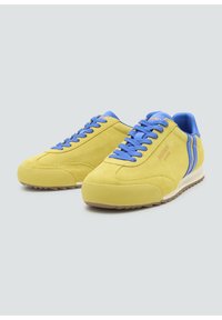 Gelbe Wildlederschuhe mit blauen Akzenten, die eine strukturierte Sohle, eine runde Zehenform und flache Schnürsenkel aufweisen. Seitliche Streifen verleihen ein markantes Detail.