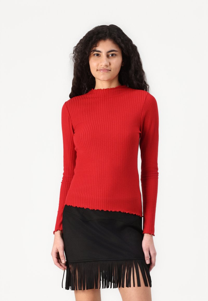 Rode geribbelde langemouwen top met een geschulpte halslijn, gecombineerd met een zwarte fringed rok, die textuur en ontwerpaccentueert.