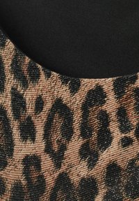 Tkanina s leopardím potiskem obsahující metalické vlákna, s texturovaným povrchem. V pozadí je viditelná černá látka.