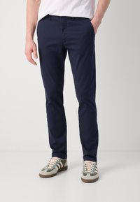 Navyn blå chinos laget av bomull med slank passform, med sidelommer og en glatt tekstur. Kombinert med lyse sneakers.
