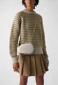 Beige crossover-taske med et glat, rundet design, der har en simpel lås og en struktureret trøje i stof med gule og grå striber.