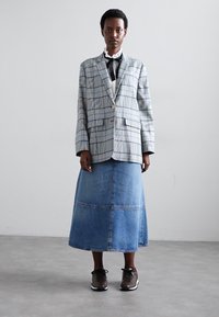Veste à carreaux oversize en bleu clair, gris et blanc ; jupe maxi en denim ; baskets brunes. Col blanc froncé sous la veste.