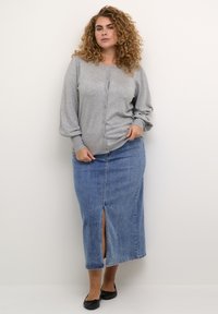 Grijze lange mouwen cardigan met knopen aan de voorkant, gecombineerd met een blauwe spijkerrok met een split aan de voorkant en zwarte platte schoenen.