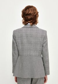 Harmaan ja mustan ruudullinen bleiseri, jossa on istuva malli. Varustettu terävällä läpällä, rakenteellisilla hartioilla ja ventiloidulla selkädesignillä.