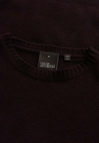 Dunkelbrauner Pullover mit einem gerippten Rundhalsausschnitt. Das Etikett trägt "OSCAR JACOBSON", Größe "M" und "MADE IN ITALY". Weiche Textur.