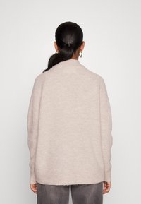 Ljust rosa, mysig stickad tröja med avslappnad passform, rundad halsringning och ribbade ärmar; parat med grå, något texturerade byxor.