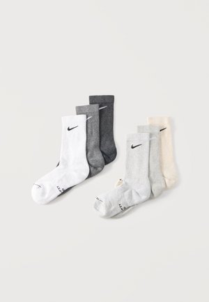 Seks Nike crew-sokker i hvid, mørkegrå, grå, lysegrå og beige, arrangeret på en ensartet lys baggrund.