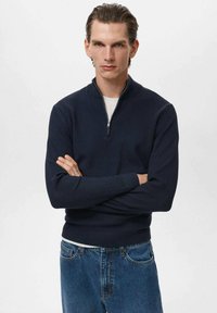 Pulover navy cu guler cu fermoar, textură côtă, mâneci lungi și siluetă ajustată, asortat cu blugi de culoare albastru deschis. Design casual și versatil.