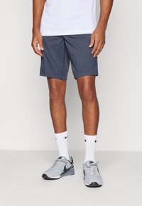 Marineblå shorts med en løstsittende passform, laget av lett materiale, kombinert med hvite Nike crew-sokker og grå treningssko.