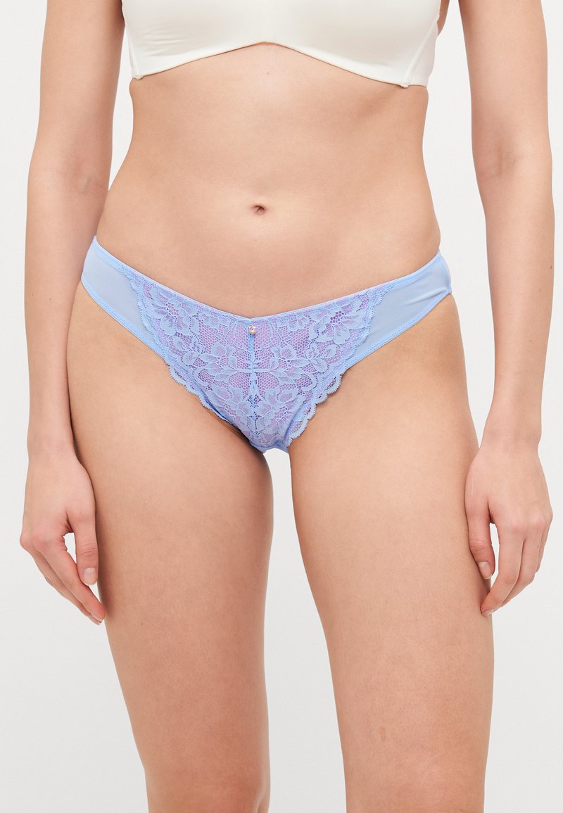Violetā mežģīņu bikini apakšveļa ar gaiši zilu satīna jostu. Ietver izsmalcinātus ziedu rakstus un nelielu dekoratīvu dārgakmeni centrā.