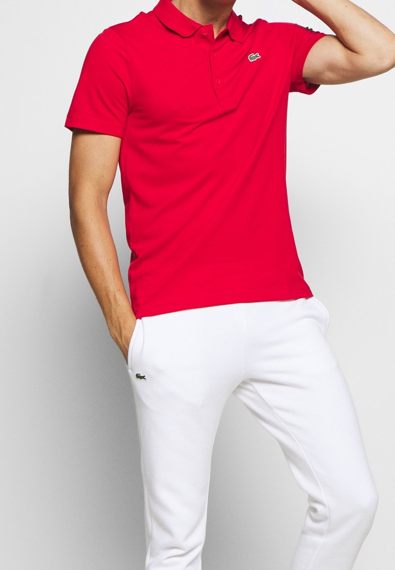 Red polo shirt made of cotton with a classic collar and short sleeves. Paired with white sweatpants featuring a small green logo.