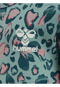 Grön texturerad tyg med rosa och marinblå leopardmönster. Har en vit "hummel"-logotyp i mitten. Avslappnad design, kortärmad.