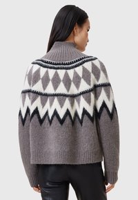 Grå stickad tröja med hög krage, med ett geometriskt mönster i vitt och svart. Mjuk textur och kort design.