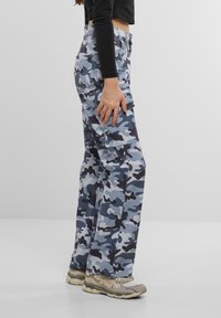 Pantalones cargo camuflados en tonos de azul y gris, con múltiples bolsillos, un corte holgado y un diseño de pierna ajustada. Combinados con zapatillas ligeras.