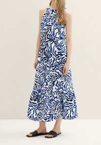 Frau trägt ein Maxikleid mit abstraktem Muster in Blau und Schwarz und schwarze flache Riemchensandalen.