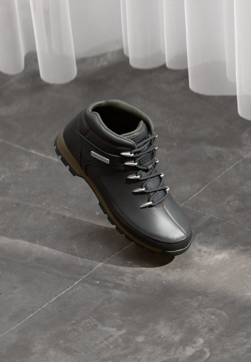 Scarpa da trekking nera con tomaia in pelle liscia, occhielli metallici e un accento testurizzato. Presenta una suola in gomma robusta per una buona aderenza.