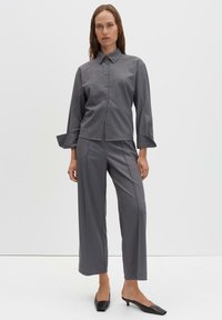 Grijs overhemd met knopen, lange mouwen en een kraag, gecombineerd met lossere grijze broek. Beide kledingstukken hebben een gladde textuur en een minimaal ontwerp.