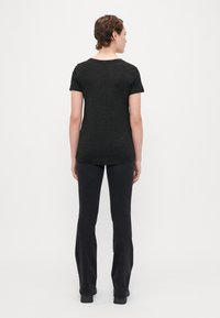 Melna īsām piedurknēm T-krekls ar teksturētu, punktētu rakstu, kombinēts ar melnām platu kāju biksēm. Apģērbs ir pieguļošā siluetā.