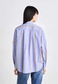 Light blue oversized shirt with vertical orange and white stripes, featuring a classic collar, buttoned cuffs, and a relaxed fit.