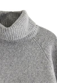 Lys grå strikket turtleneck sweater med ribbet krave og fin strikketekstur, der viser skuldersømmen og øvre brystområde.