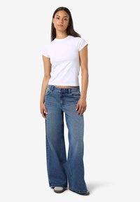 Λευκό κοντομάνικο εφαρμοστό T-shirt συνδυασμένο με φαρδύ μπλε τζιν παντελόνι που διαθέτει ανοιχτό χρωματισμό και μπροστινές τσέπες.