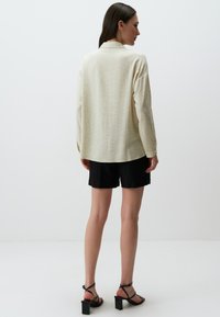 Crème, languit-shirt met een subtiele textuurpatroon, gecombineerd met zwarte shorts en zwarte haksandalen. Schone, minimalistische stijl.