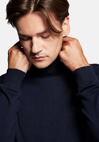 Granatowy sweter z golfem o prążkowanej teksturze, dopasowanym kroju i długich rękawach. Posiada subtelne logo na piersi. Wygląd miękkiej tkaniny.