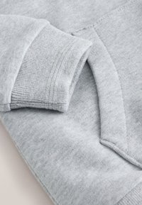 Zbliżenie jasnoszarej bluzy pokazującej prążkowany mankiet i krawędź kieszeni kangurka.